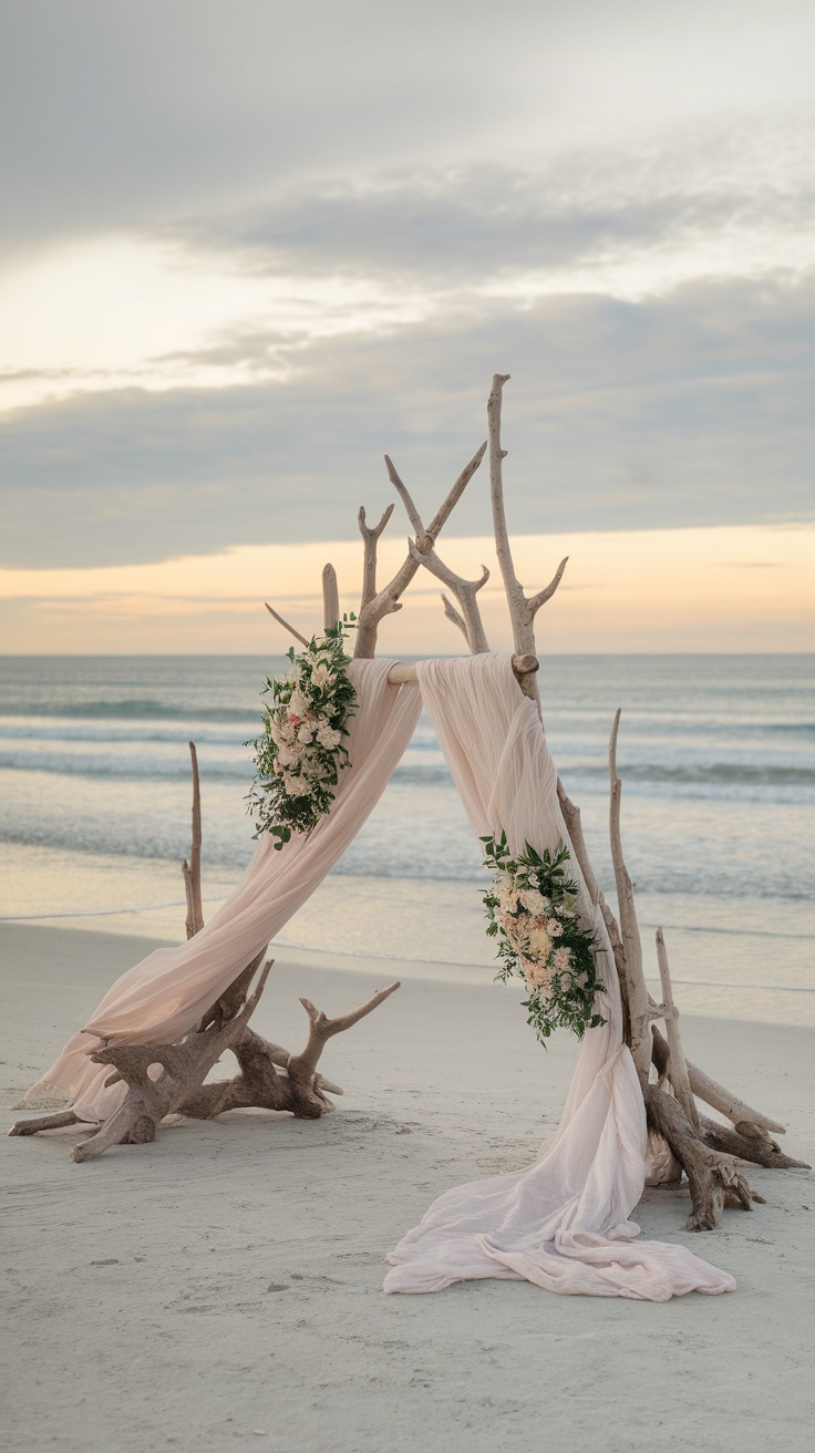 Driftwood altar backdrop with flowers and draped fabric on the beach.