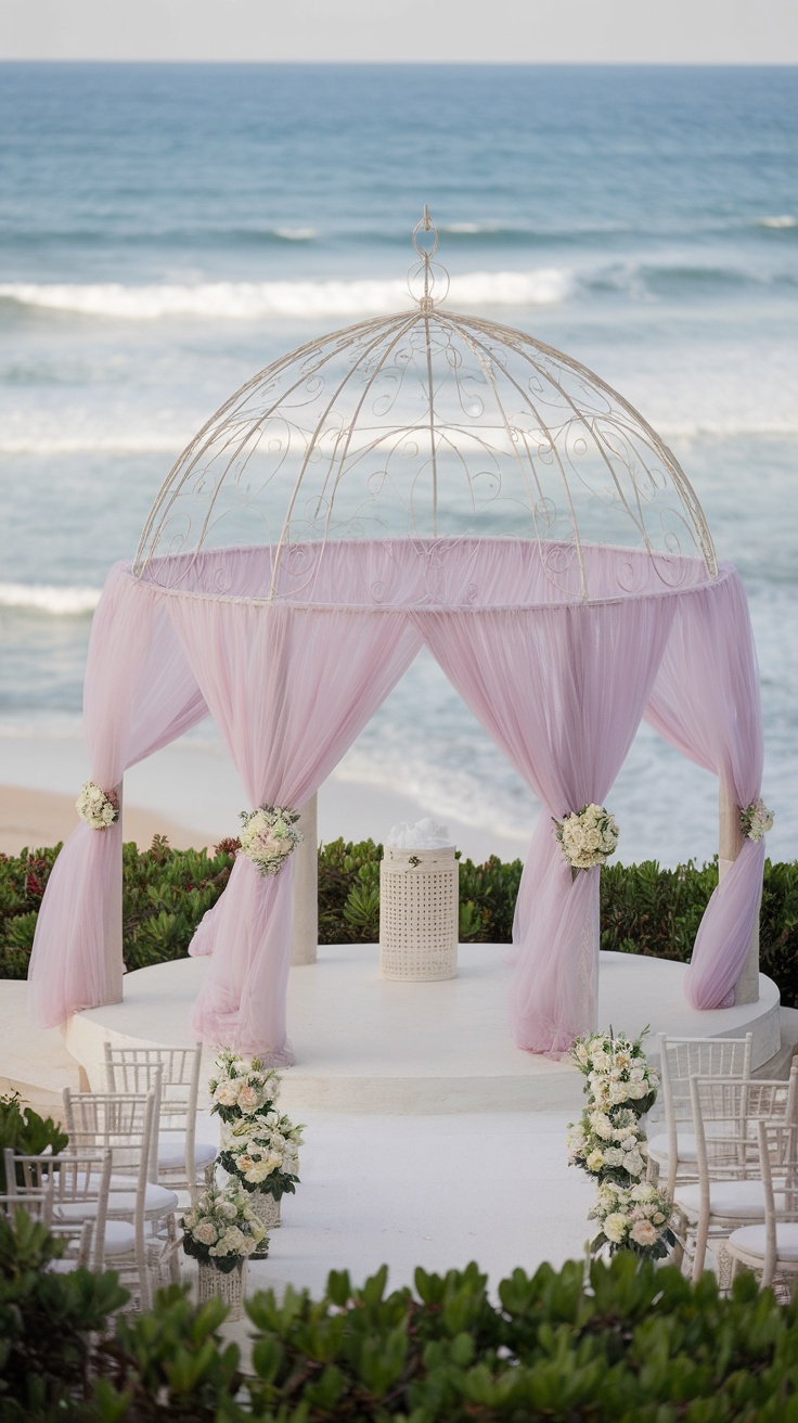 A beach wedding gazebo draped with pink tulle and adorned with floral arrangements