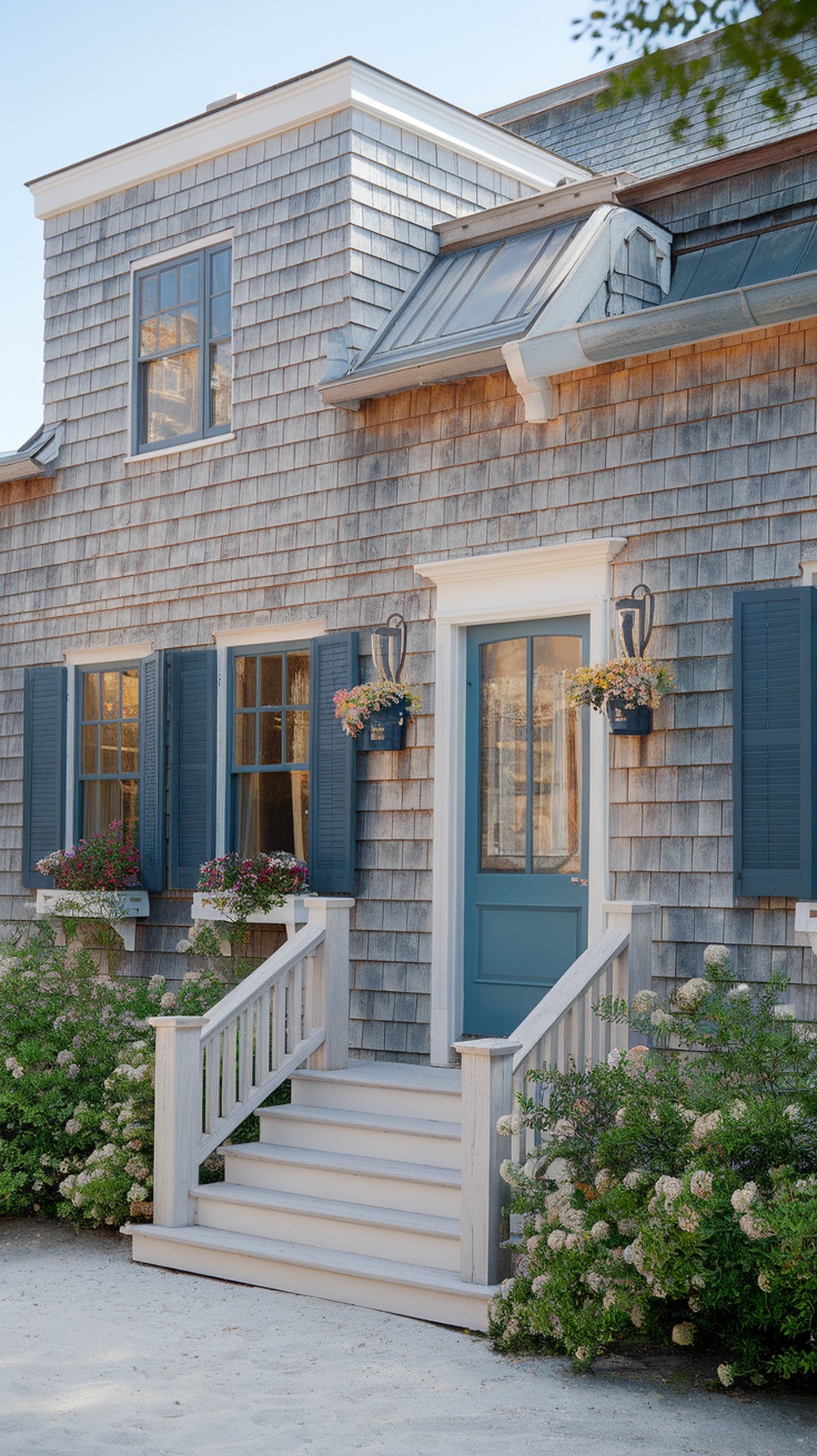 Classic shingle style architecture of a Nantucket home featuring wooden shingles, a blue door, and flower-filled window boxes.