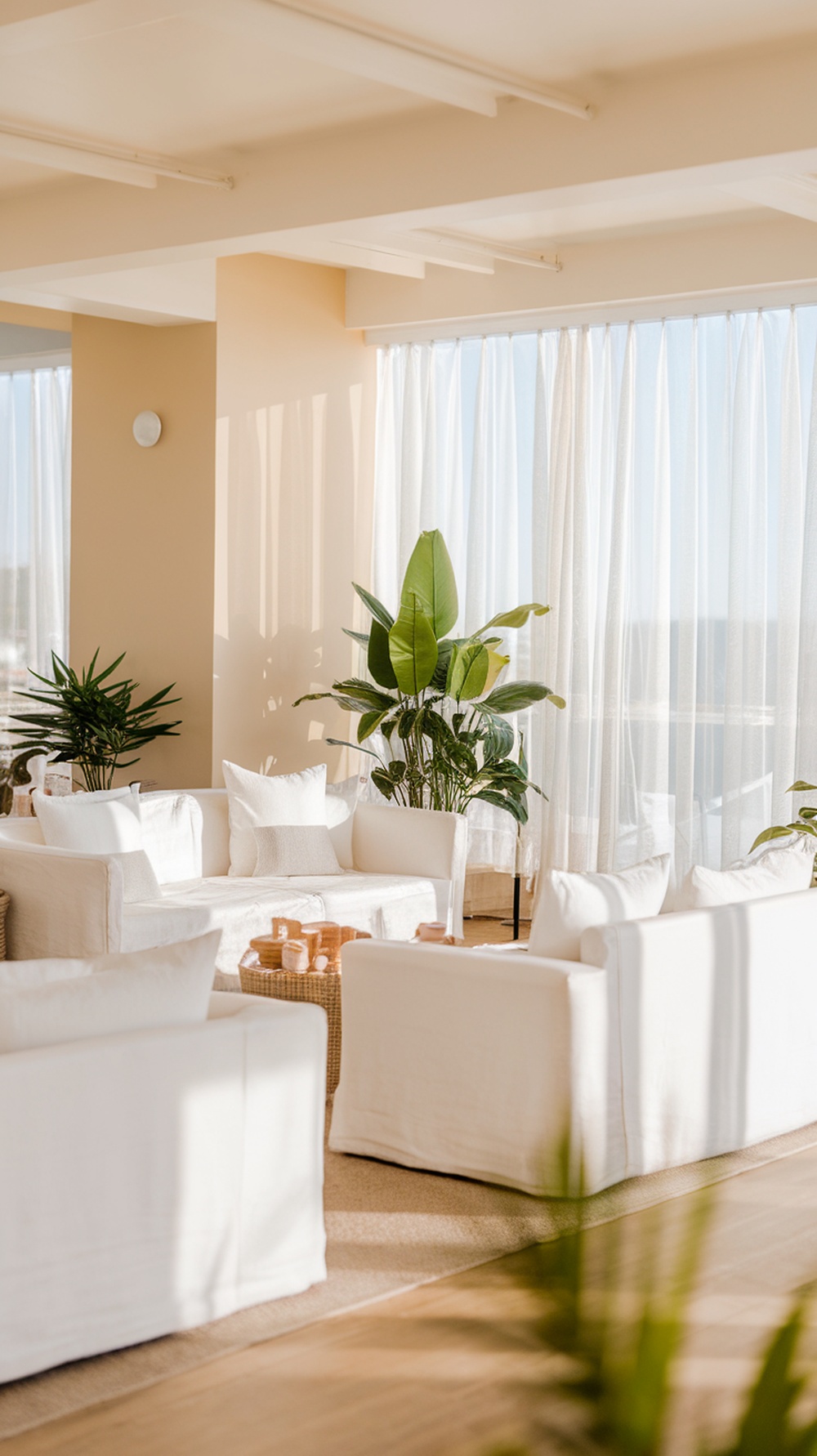 Bright modern coastal living room with large windows, white furniture, and indoor plants.